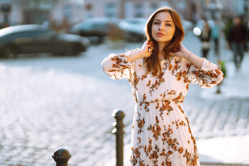 The portrait of young stylish woman in fashion dress posing at sunset in the city. Lifestyle...
