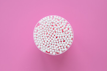 A cotton buds for cleaning ears in round container on pink background, top view. Hygienic sticks for cosmetic procedures.