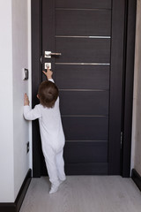A small child tries to leave the room. A baby in a white jumpsuit stands at the door. Home...