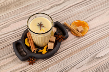 Masala tea in a glass cup on a wooden table, top view. Original serving on a wooden plate with...