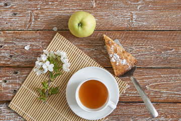 Homemade apple pie with cinnamon and cup of tea on wooden table.