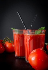glasses of tomato juice with mint and tubes, fresh red tomatoes on a black