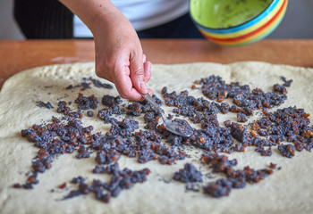 Cooking delicious sweets with jam and powder to tea.Top view. Womans hands are preparing a cake by adding dough. On a brown table lies a few dough. Sunny morning.