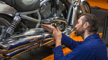 Close up photo of a man repairing bike. Young man repairing motorcycle in workshop.