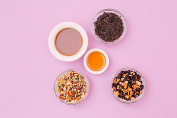 Obraz na płótnie Canvas Flat lay with cups full with different types of teas, and mixed dried fruits, isolated on a pink background. 