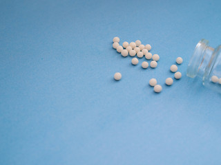 Fototapeta na wymiar Homeopathic globules and glass bottle on blue background. Homeopathic Medicine