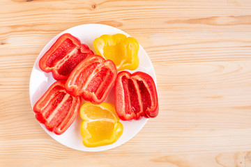 Red and yellow pepper sliced on plate on wooden background