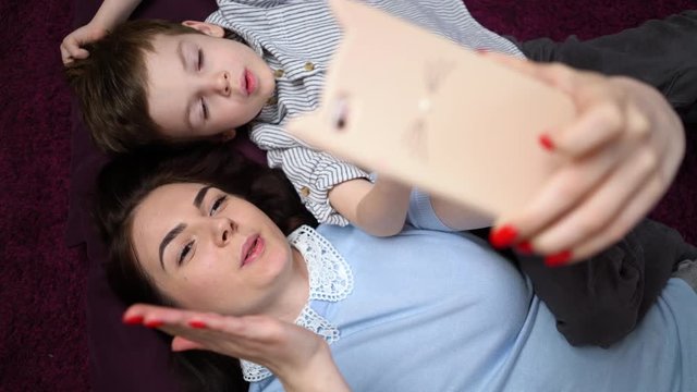 mother and her son making a selfie or video call to father or relatives on the carpet. Vertical video