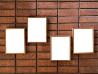 Four white blank picture frames hanging on the red brick wall background.