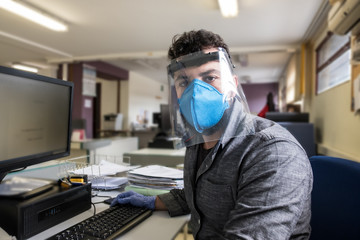 Fototapeta na wymiar Man with protective screen and facial mask working at office