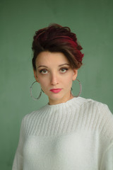 Attractive young woman with perfect skin and makeup is possing on green background in studio wearing white sweater and silver earrings