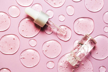 Liquid gel or serum drops with pipette on pink background in macro. Flat lay style.