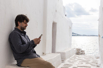 Fototapeta na wymiar Young man using mobile phone sitting on a white wall