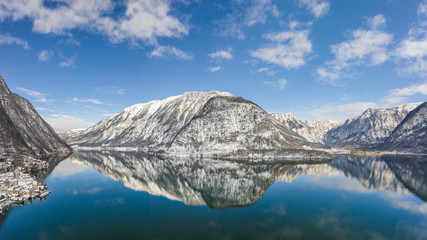Obraz premium Aerial drone shot of snow covered hill with reflection by Hallstatt lake in Austria during winter time
