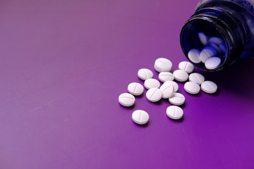 bottle of white pills on purple background 