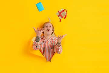 Gifts giving. Cheerful caucasian young man poses in torn yellow paper background, emotional and expressive. Breaking on, breakthrought. Concept of human emotions, facial expression, sales, ad.