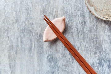 Wooden chopsticks and chopstick rest on rustic wooden background. Top view. Copy space.