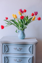 Bouquet of colorful tulips in a vase on a vintage blue nightstand. Isolated on white background
