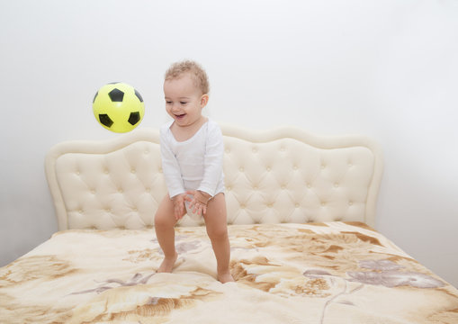 2 Year Old Boy Playing With Ball On Parents Bed