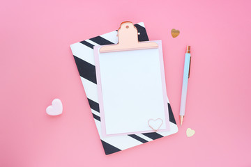 Mock up pink clipboard, pen, paper clip, striped notebook and hearts on a pink background. Space...