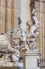 Fototapeta na wymiar Fancelli's ancient lion - Medici lion. Marble sculpture displayed at the Loggia dei Lanzi. The Rape of the Sabine Women on background. Piazza della Signoria, Florence, Italy. Focus on foreground.