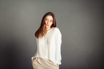 Young girl in a white shirt on a gray background. French woman in white blouse against a background of gray walls. Without retouching. Without make-up.