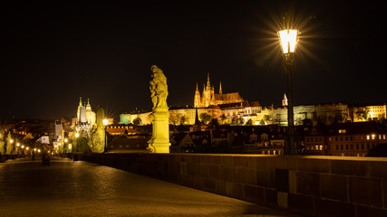 Panoramic view of Prague skyline at night. Statues and gas lamps on the Charles bridge and Prague Castle with spires of St. Vitus cathedral in background