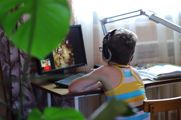 a boy with headphones at home sits at a computer and learns remotely