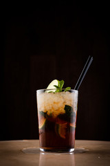 Alcoholic mojito with lime and mint on dark background. Mojito with black straw in glass cup. General shot