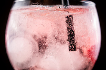 A black straw stirring a pink gin tonic with strawberries on a black background. The black straw...