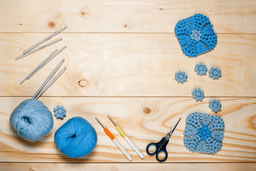 Accessories and tools for knitting, colored yarn, crochet blue square patterned napkins, hooks, scissors on light wooden background close-up top view with copy space and place for text
