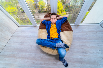 Boy resting at balcony during isolation. Quarantine at home for children. Boy relaxing in soft chair.