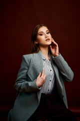 Independent young woman posing in the photostudio. Gorgeous young female in classic suit and grey coat.