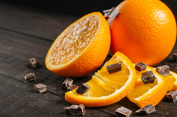 Whole, half of an orange and sliced fresh juicy orange with chocolate on a dark brown wooden background