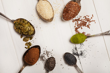 Superfoods in metal spoons on a white wooden background. Top view