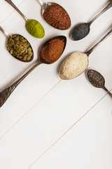 Superfoods in metal spoons on a white wooden background. Top view