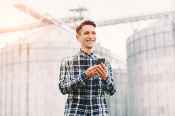 Portrait of happy young agriculture business owner holding mobile phone and smiling while standing...