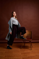 Independent young woman posing in the photostudio. Gorgeous young female in classic suit and grey coat.