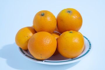 Many oranges are in a ceramic dish, fruit rich in juice and vitamin c.