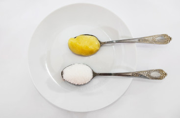 sugar and honey in spoons in a white plate. The concept of choosing between sugar and honey. View from above.