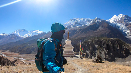 A man hiking next to a stupa with snow caped Annapurna chain in the back, Annapurna Circuit Trek, Himalayas, Nepal. High mountains around. Some prayer's flag next to it. Serenity and calmness.