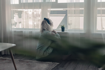 Lady sits in front of large window on the floor. Social distancing. Self isolation, stay at home...