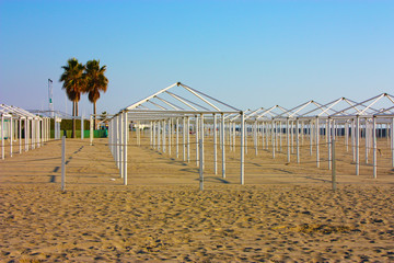 structures for desolate umbrellas and tents of unused bathing establishments alone without quarantine on the beach by the sea