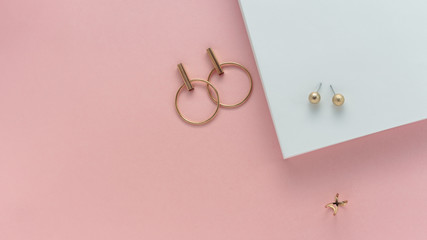 Golden stud earrings and golden ring on white and pink paper background with copy space