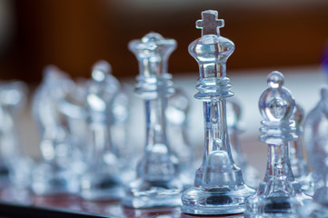 Close-up of a transparent king chess piece sitting on a chessboard. Shallow depth of field.