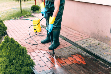Man cleaning red concrete pavement block using high pressure water cleaner. Paving cleaning...