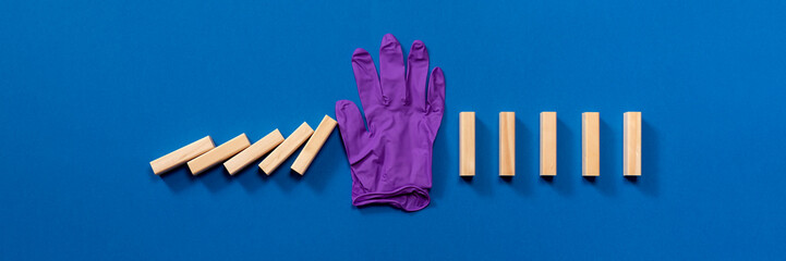 A surgical glove stops the pieces of domino wood from collapsing. Visual scheme that explains the importance of maintaining good hygiene between people to avoid contagion by viruses.