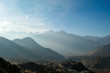 Himalayan chains shrouded in fog, seen from Muktinath, Annapurna Circuit Trek, Nepal. There are multiple mountain chains. Sunbeams breaching through the peaks. Golden hour. Meditation and serenity.