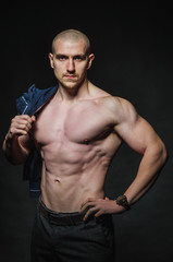 Fototapeta premium A stylish, bald young man stands with a naked torso on a dark background in the category