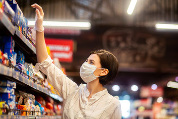 Young woman shopping in supermarket with shopping cart wearing medical face mask to protection the COVID-19 virus.